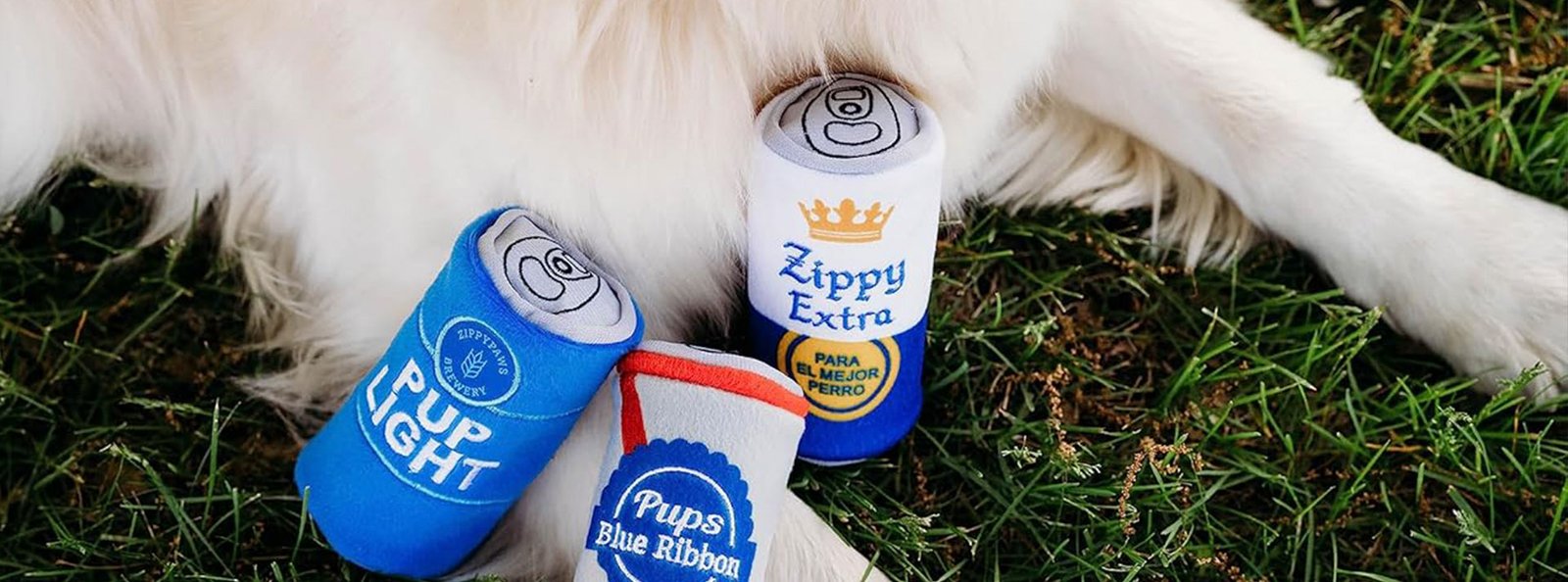 A dog’s paws beside three beer can toys labeled ‘Bark Light,’ ‘Zippy Extra,’ and ‘Pupps Blue Ribbon’ on a grassy background