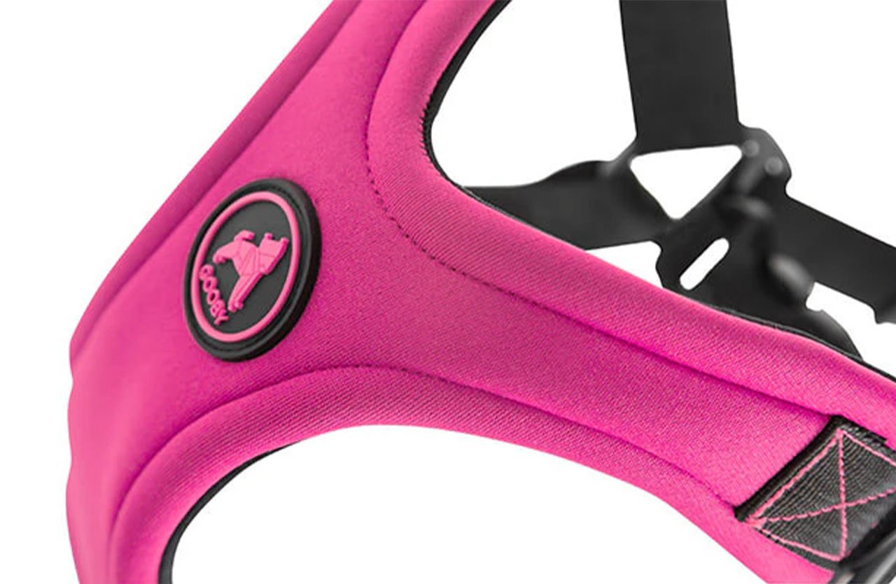 Close-up of a pink neoprene dog harness with a circular logo, showcasing its tough, all-weather resistant material.