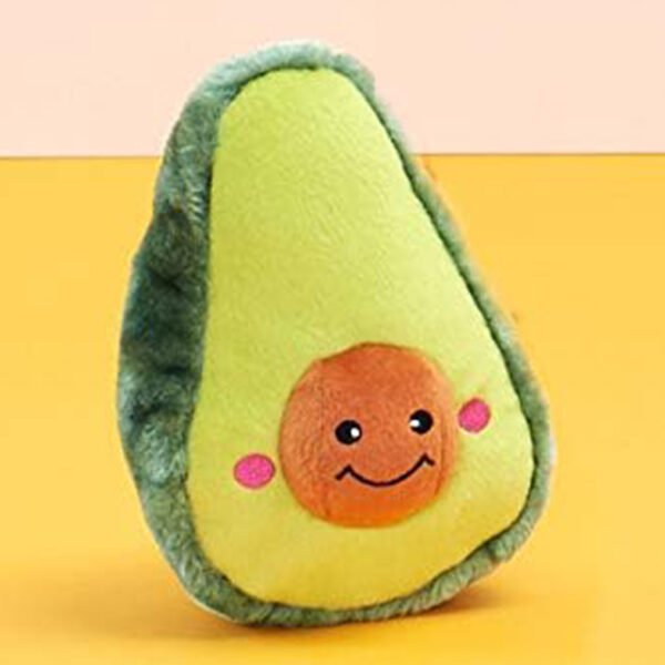 Soft avocado-shaped plush toy with a smiling face, standing upright against an orange and pink gradient background