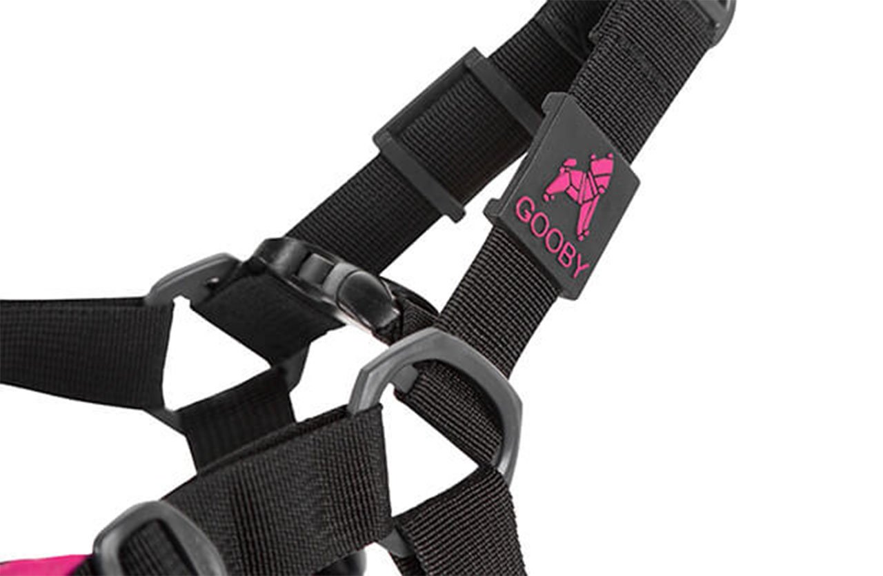 Close-up of a black strap with a sizing adjustment tab and a pink Gooby logo, ensuring a firm fit around the chest.