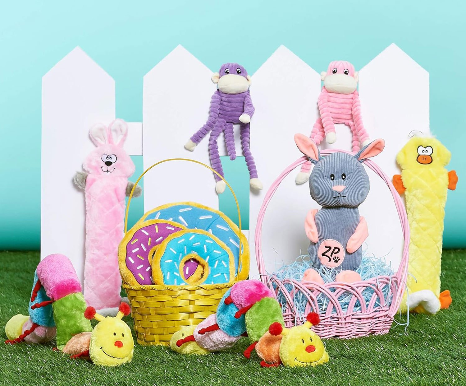 Variety of plush toys arranged in front of a white picket fence with green grass and a light blue background