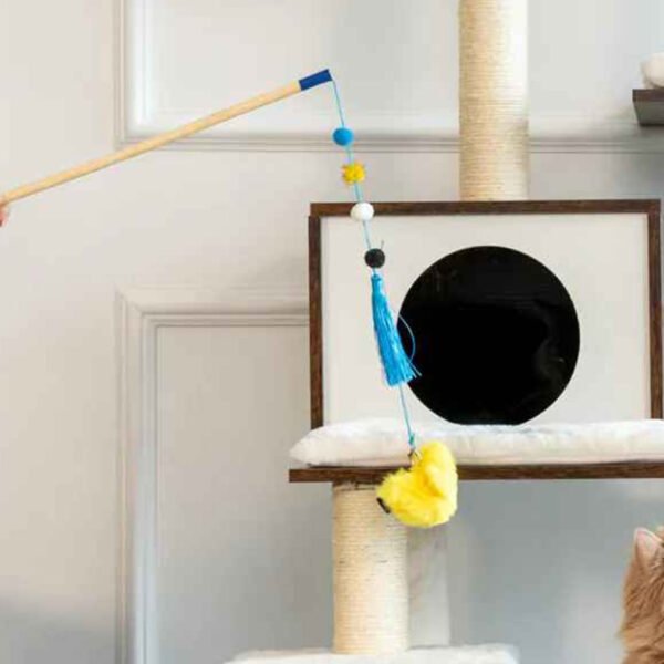 A cat gazes at the ZippyStick Bird, an interactive cat toy wand featuring a blue feather, beads, and a yellow fluff on a string, held by a person against a home interior background.