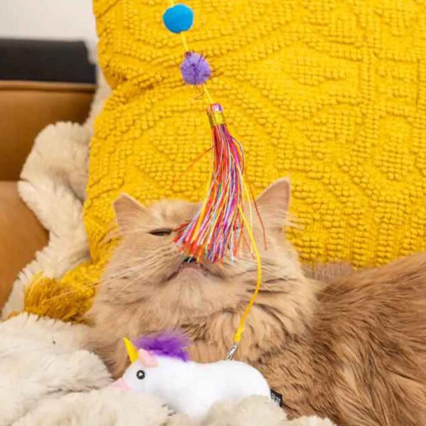 An orange cat engaging with a ZippyStick Unicorn cat toy wand, featuring vibrant multicolored ribbons and a plush unicorn attachment.