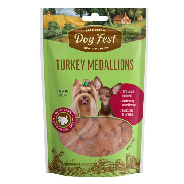 A package of “Dog Fest Treats & Chews Turkey Medallions” featuring an image of a farm with a red barn and green fields in the background, alongside two happy small breed dogs. The package is predominantly green and brown with a clear window showing the turkey medallion treats inside.