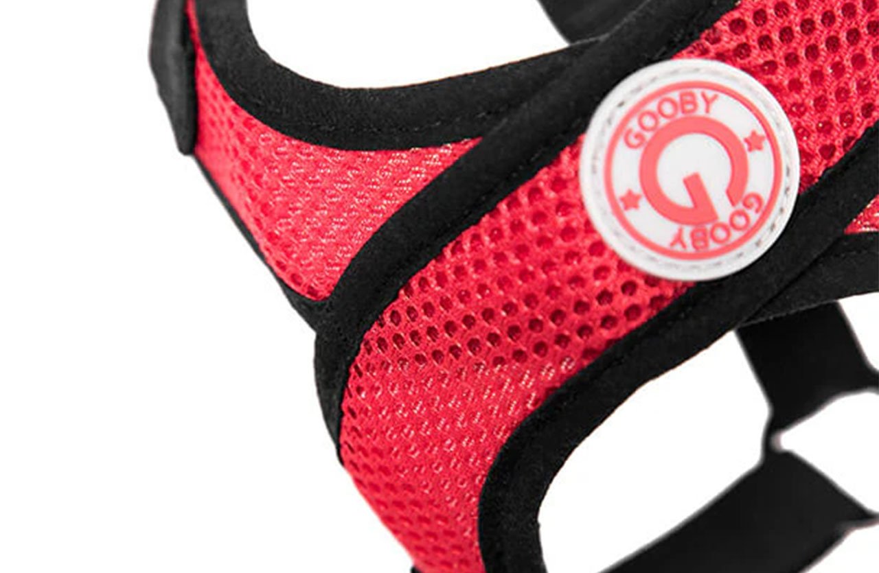 Close-up of red mesh fabric with a honeycomb pattern, part of the Comfort X Step-In Harness, featuring solid black edging and a circular “GOOBY” logo patch.
