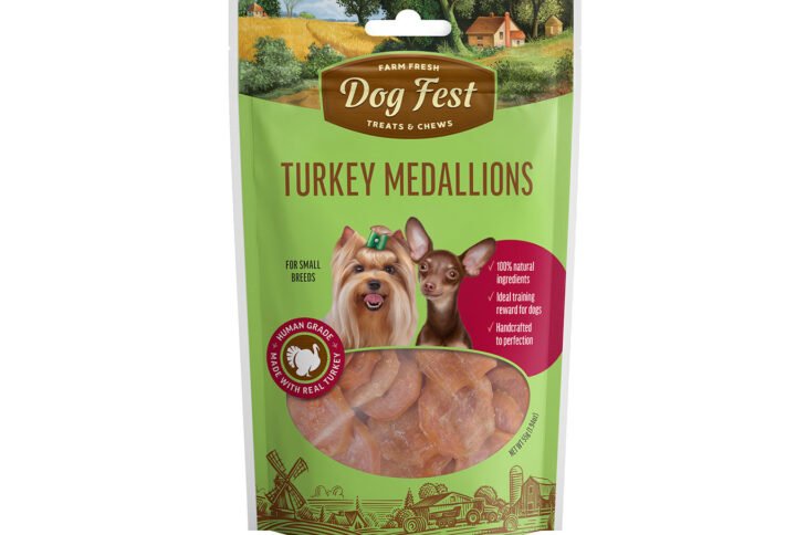 A package of “Dog Fest Treats & Chews Turkey Medallions” featuring an image of a farm with a red barn and green fields in the background, alongside two happy small breed dogs. The package is predominantly green and brown with a clear window showing the turkey medallion treats inside.